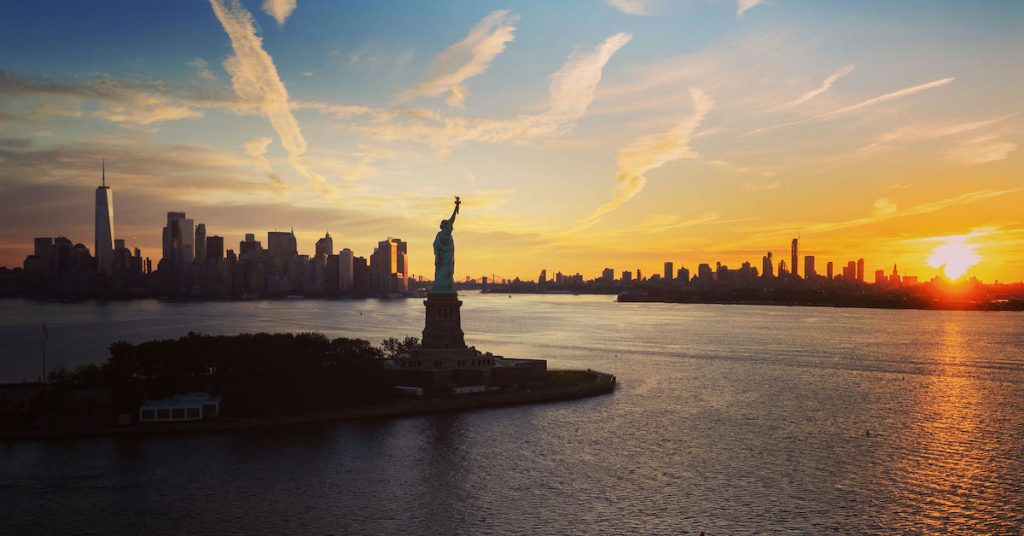 The Statue of Liberty at sunrise with the Freedom Tower and Manhattan in the background.